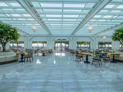 Bright hotel lobby with marble floor, glass ceiling, and green plants.
