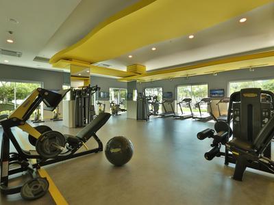 Modern gym with workout machines, large window, and yellow ceiling in a hotel.