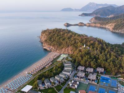 Coastal hotel with pools near a forest and sandy beach by calm sea.