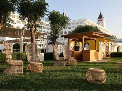 Hotel garden with shade trees, many wicker chairs, and a small yellow pavilion.