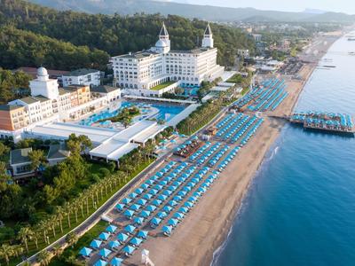 Luxury hotel with pools and sun loungers on a long sandy beach beside blue sea.