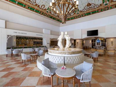Spacious hotel lobby with marble flooring, circular seating, and central sculpture beneath ornate glass ceiling.