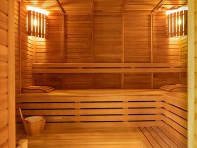 Wooden sauna with two tiers, wooden benches, bucket, and warm lighting.