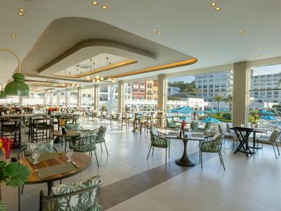 Modern restaurant overlooking large outdoor pool and hotel in sunny setting.