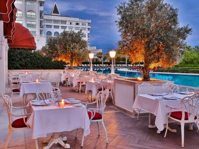 Hotel terrace with white tables and chairs beside a lit pool at dusk.
