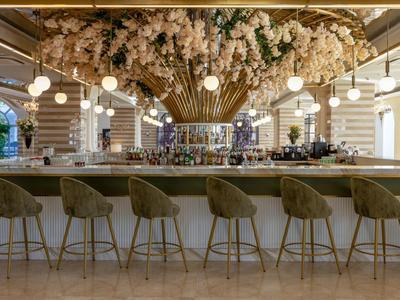 Elegante Hotelbar mit hoher Decke, runden Hockern und blumenverziertem Kronleuchter.