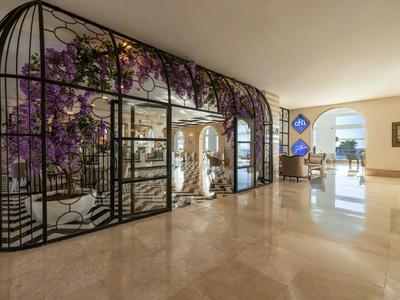 Moderne Hotellobby mit Glas- und Metallstruktur, die lila Blumen zeigt.