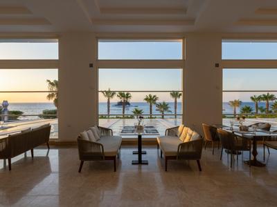 Offener Hotel-Loungebereich mit Blick auf das Meer und Palmen bei Sonnenuntergang.