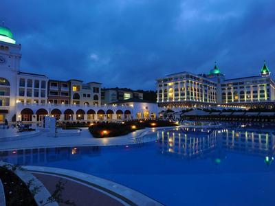 Hôtel luxueux avec façades éclairées et grande piscine dans le crépuscule bleu du soir.
