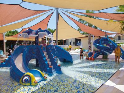 Area giochi colorata per bambini con fontane d'acqua e vele ombreggianti in un'area esterna dell'hotel.