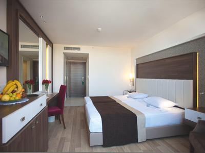 Camera d'hotel moderna con letto matrimoniale, TV, area salotto e scrivania con cestino di frutta.