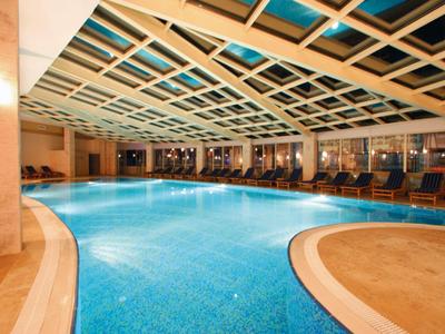 Piscina coperta con acqua blu, comode sdraio e grandi finestre in un hotel.