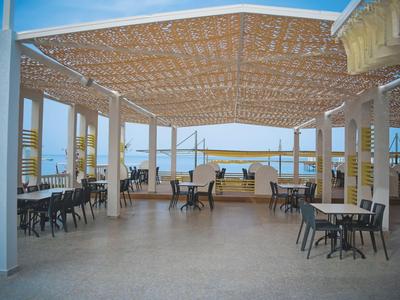 Open overdekte eetruimte met tafels en stoelen, uitzicht op zee.