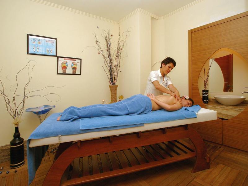 Un uomo riceve un massaggio in una stanza luminosa con un lettino da massaggio e piante decorative.