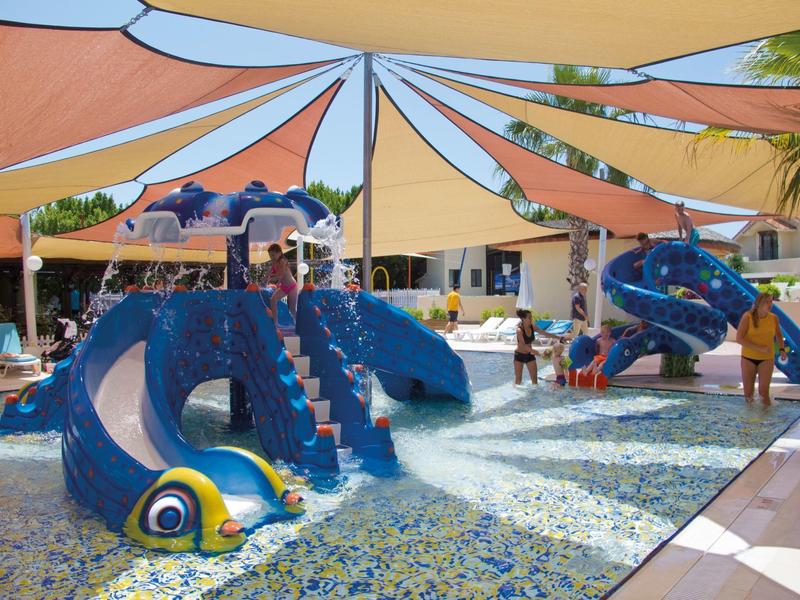 Area giochi colorata per bambini con fontane d'acqua e vele ombreggianti in un'area esterna dell'hotel.