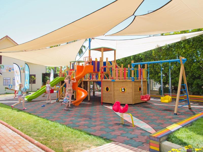 Parco giochi colorato con scivolo, altalene e struttura per arrampicata sotto tende da sole