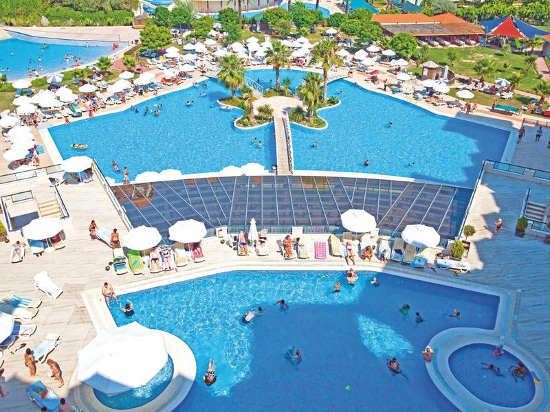 Grande piscina dell'hotel con ombrelloni, sdraio e ospiti, circondata da paesaggio tropicale.