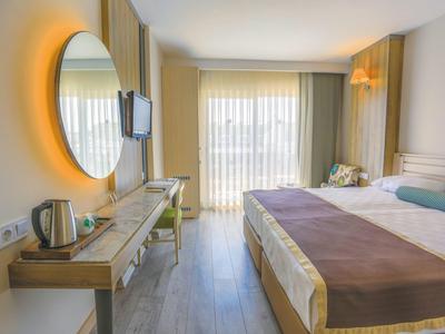 Camera d'hotel luminosa con letto grande, specchio illuminato e balcone con tende.