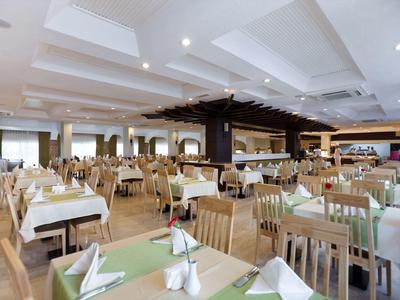 Ampia sala da pranzo luminosa con sedie in legno e tovaglie bianche in un hotel.