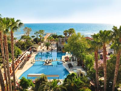Großer Hotelpool mit Sonnenliegen und Palmen, Blick auf das Meer im Hintergrund.