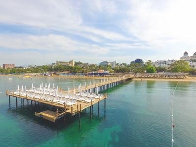 Langer Steg mit Sonnenschirmen über klarem Meerwasser an einem Strand mit Gebäuden im Hintergrund.