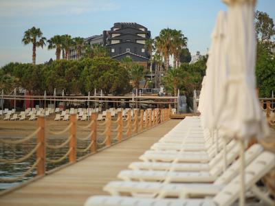 Ampio pontile con lettini bianchi e ombrelloni sulla spiaggia, palme sullo sfondo.