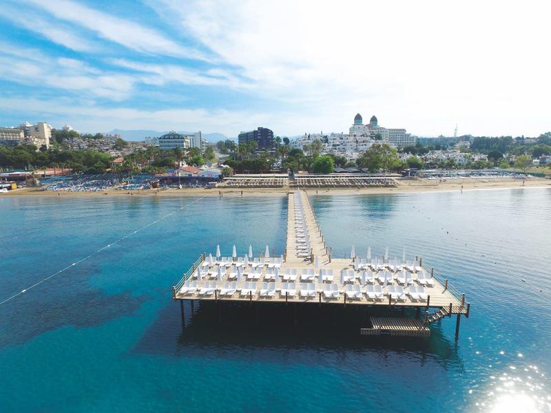 Lunga passerella con lettini sull'acqua calma davanti a una città costiera.