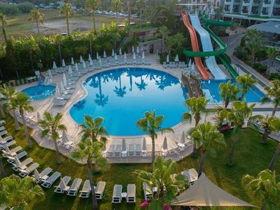 Großer Hotelpool mit Wasserrutschen, umgeben von Sonnenliegen und Grünflächen.