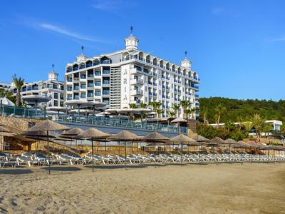 Großes Hotel am Strand mit Liegestühlen und Sonnenschirmen unter klarem blauem Himmel.