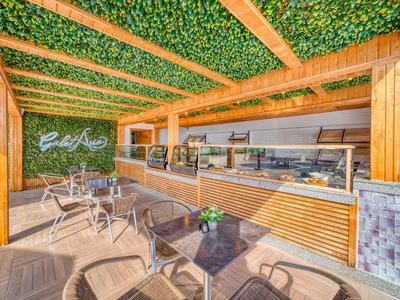 Moderner Außenbereich mit Holzstruktur, grünem Dach und Sitzgelegenheiten neben einem Bistro.