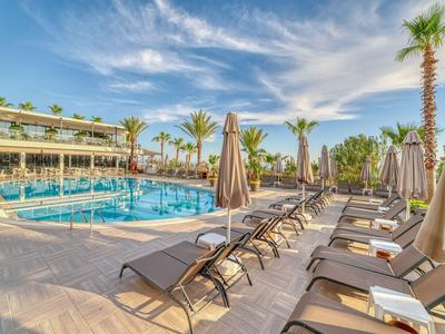 Moderner Hotelpool mit Liegestühlen und Palmen unter blauem Himmel.