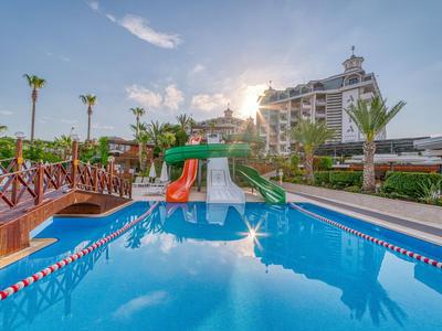 Ein blauer Pool mit bunten Wasserrutschen und einem Hotelgebäude im Hintergrund bei Sonnenuntergang.