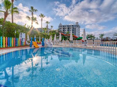 Großer Hotelpool mit Sonnenliegen und Palmen unter blauem Himmel.