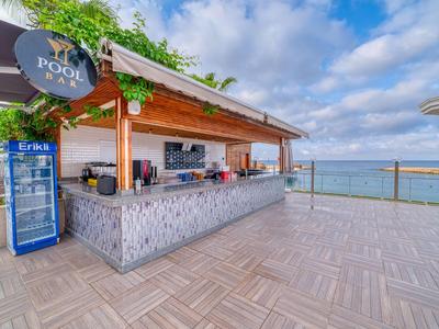 Moderner Poolbarbereich mit Holztheke und Meerblick bei klarem Himmel.