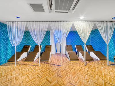 Ruheraum mit braunen Liegen, weißen Vorhängen und blau gemusterten Wänden in einem Hotel.