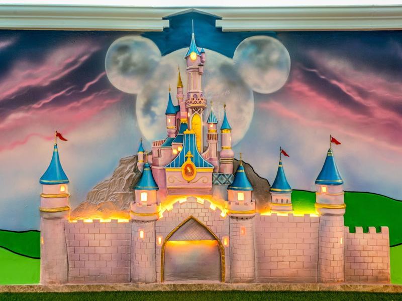 Un château illuminé avec des tourelles bleues et un nuage en forme de Mickey Mouse dans le ciel.