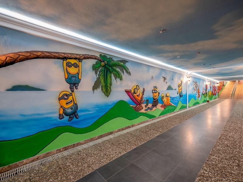 Couloir souterrain bien éclairé avec une fresque colorée accueillant les visiteurs.