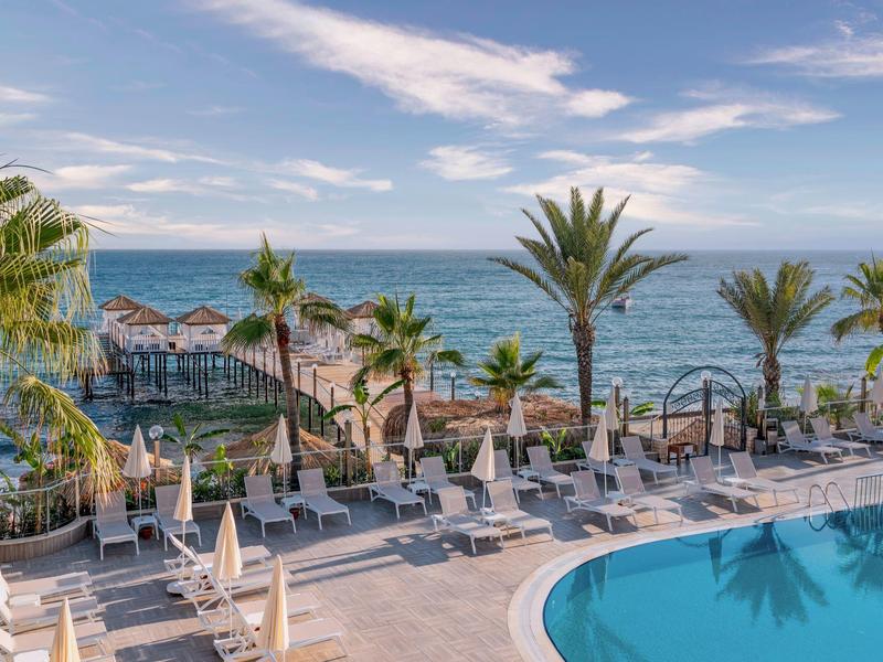 Piscine d'hôtel avec chaises longues, palmiers et vue sur la mer sous un ciel bleu