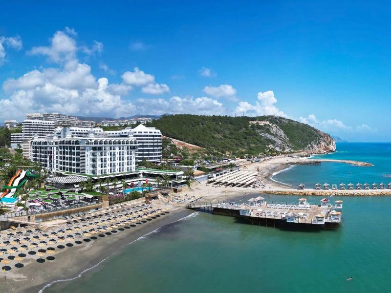 Vue aérienne d'un hôtel en bord de mer avec piscine, transats et port abrité.