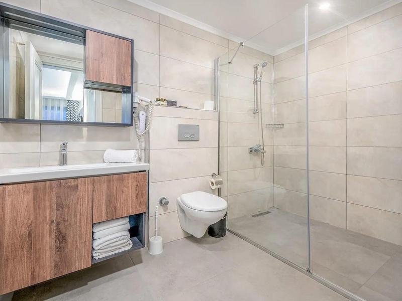 Salle de bain moderne avec grande douche en verre, toilette suspendue et meuble sous-vasque en bois.
