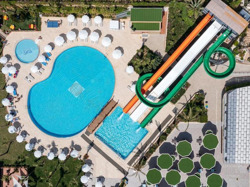 Vue aérienne d'une piscine de complexe hôtelier avec toboggan et parasols.