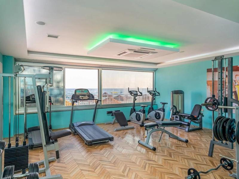 Salle de sport lumineuse avec divers équipements et grandes fenêtres donnant sur l'extérieur.