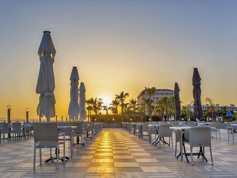 Terrasse extérieure vide d'un restaurant au coucher du soleil avec parasols fermés et tables.
