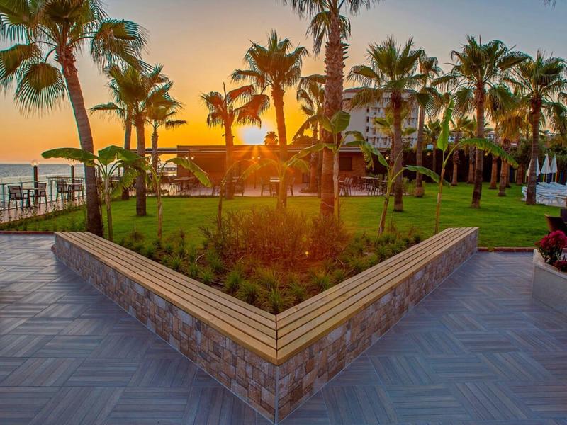 Coucher de soleil sur un jardin d'hôtel avec des palmiers et une ambiance calme au bord de la mer.