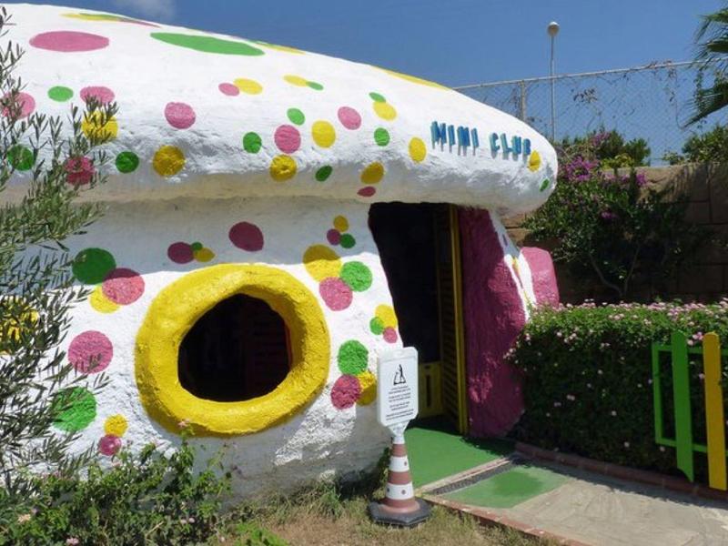 Bâtiment en forme de champignon décoré coloré avec fenêtre jaune et porte sous un ciel bleu.