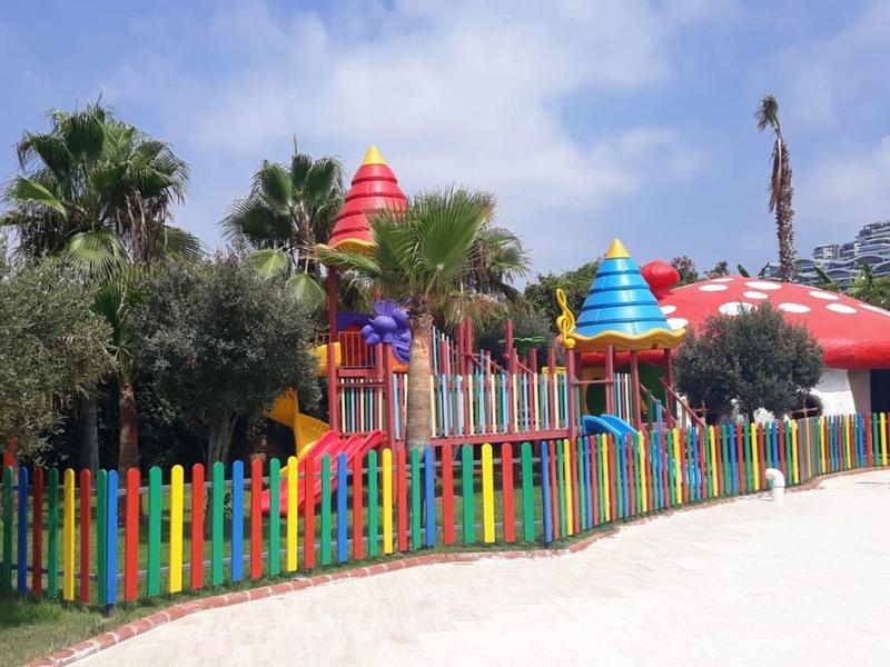 Aire de jeux colorée avec clôture et toboggans dans un cadre hôtelier tropical.