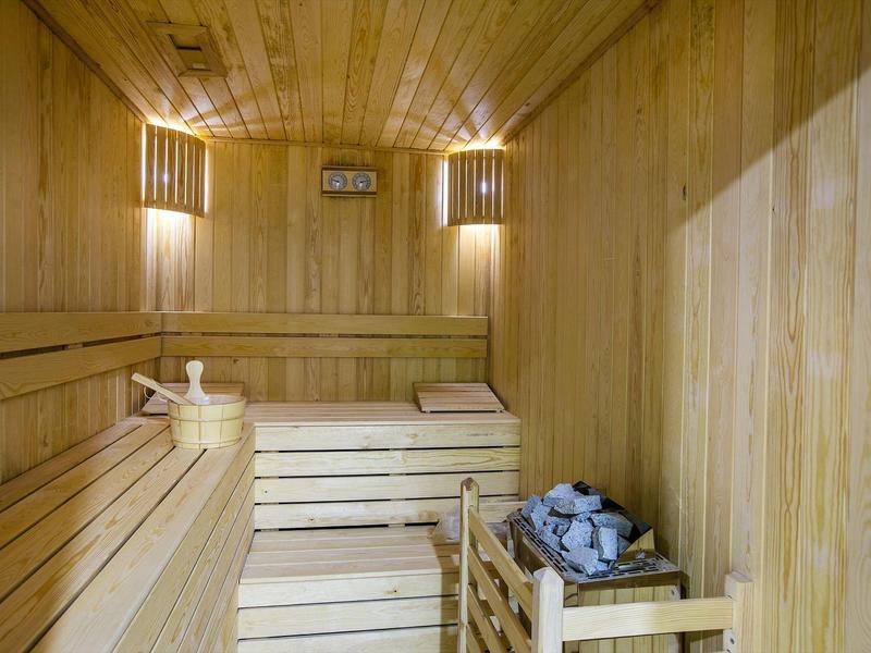 Sauna en bois avec bancs, seau et louche, éclairé par des appliques murales.