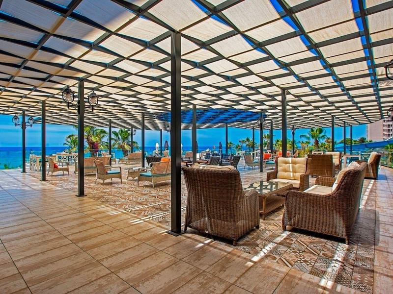 Salon couvert avec fauteuils en osier et vue sur la mer dans un hôtel.