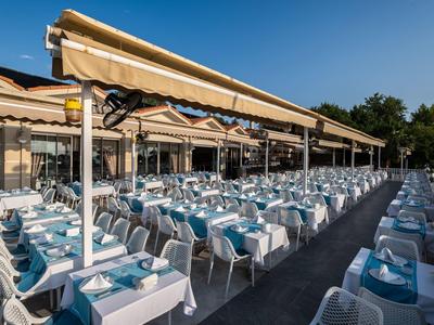 Groot buitenterras van restaurant met gedekte tafels onder zonneschermen overdag.