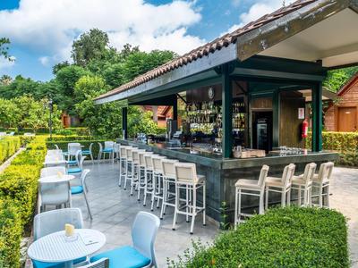 Area bar esterna moderna con posti a sedere e verde sotto il sole.